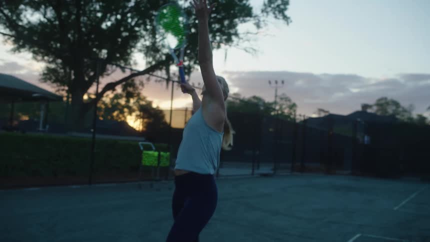 Woman throwing a tennis ball with a racket on a court in the late afternoon