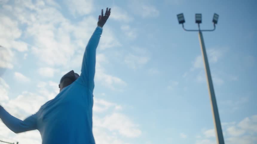 A tennis player serves a ball under a blue sky