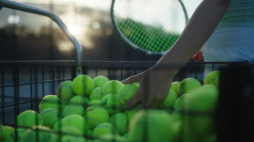 A woman takes tennis balls from a basket in the court at morning practice