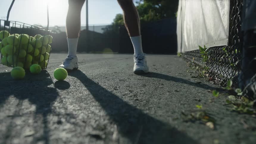 A tennis player walks the court picking up tennis balls