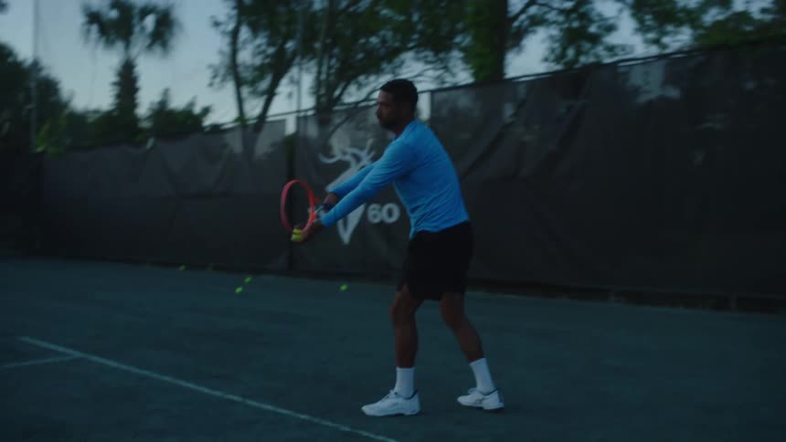 Male tennis player on tennis court bounces ball before serving it