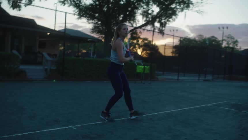 Woman plays tennis outdoors at dusk