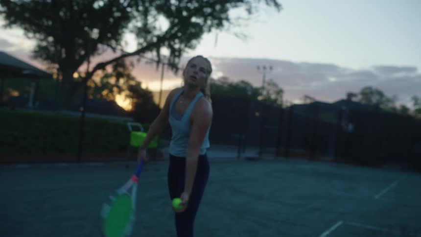 Blonde tennis player serves tennis ball at sunrise