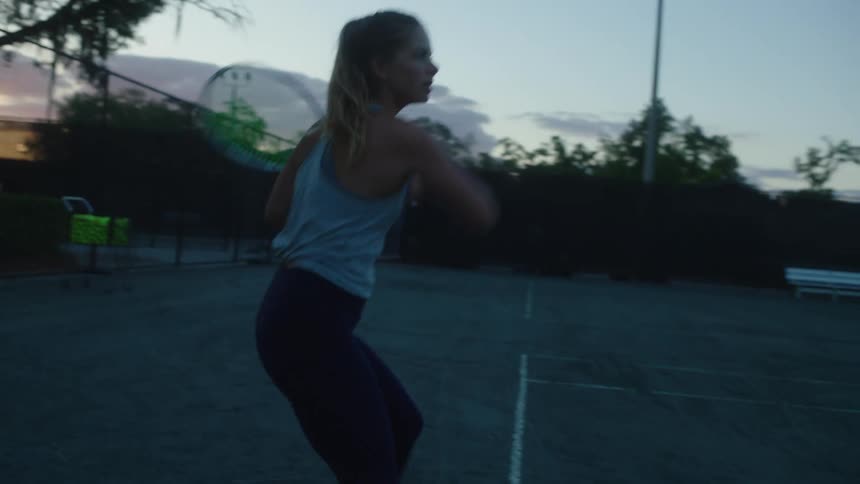 Woman with a racket playing tennis on a court in the late afternoon