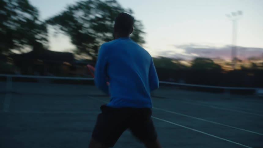 A male tennis player hits balls over the courts net