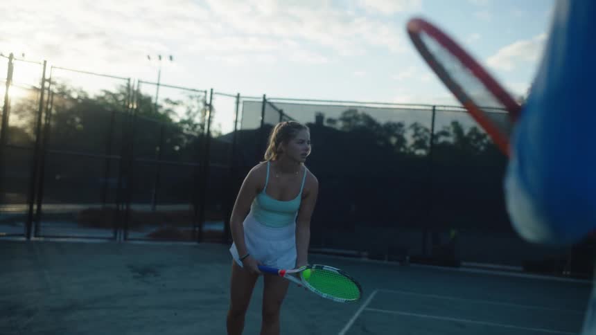 Woman practicing a serve on a tennis court with a man beside her watching