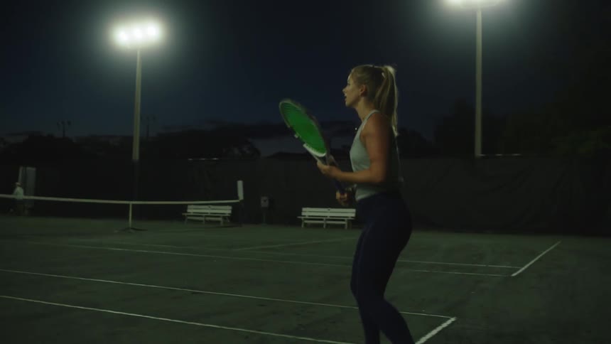 A blonde woman is playing tennis on a court and is hitting the ball with her racket