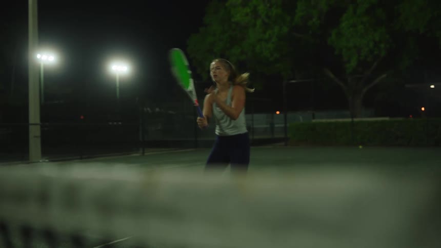 A woman playing tennis on a tennis court at night