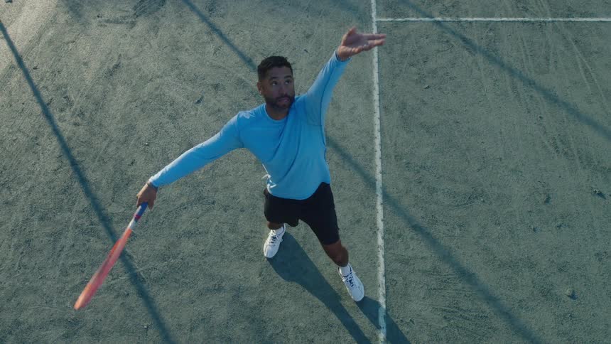 A man playing tennis serves a ball in the court