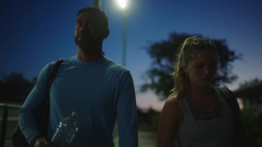 Sweaty man and woman walking side by side with tennis equipment