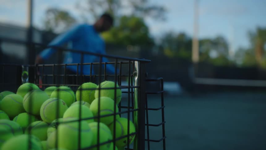 Basket with tennis balls and a man with a racket playing right in front