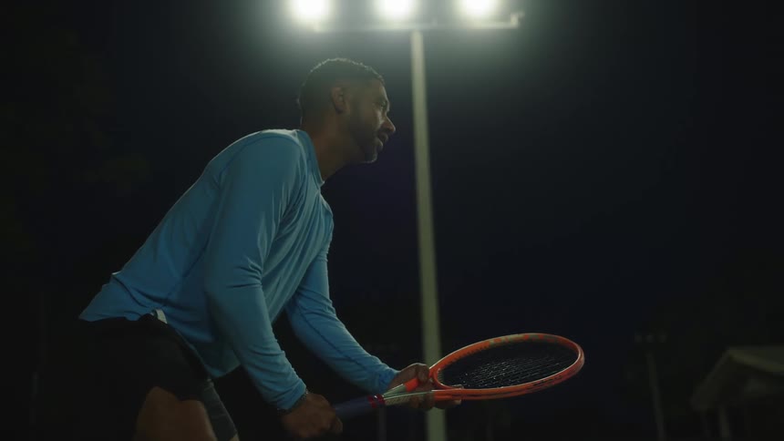 A male tennis player stands ready on the court with a racket