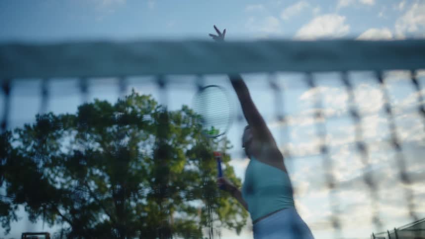 A female tennis player seen behind a net returns a ball to the other side of the court