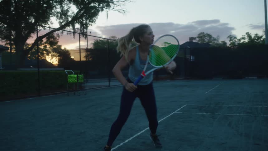 A blonde woman is playing tennis against a person and she is focused