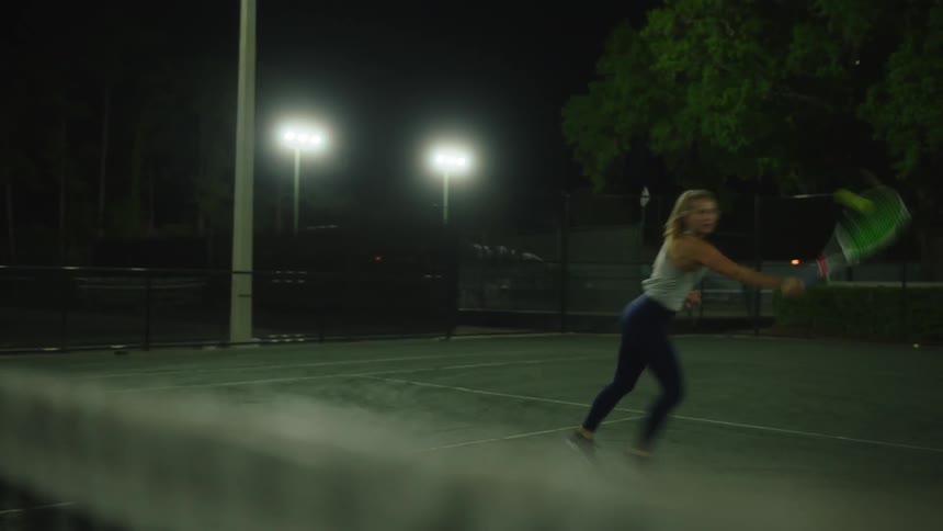 A woman playing on a tennis court at night