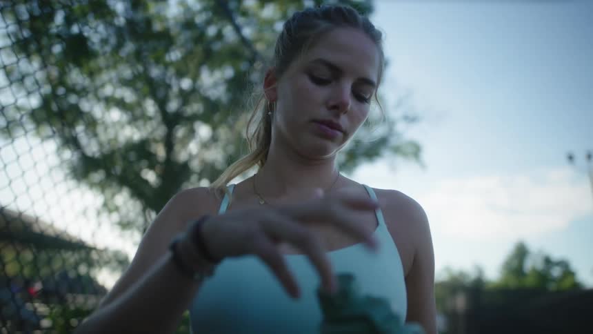 A female tennis player drinks from a thermos in the court at morning