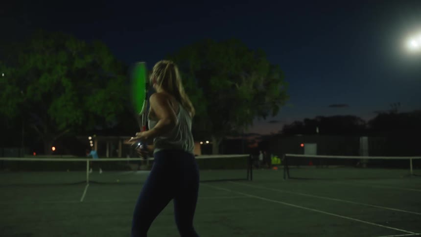 Blonde woman on a tennis court playing at night
