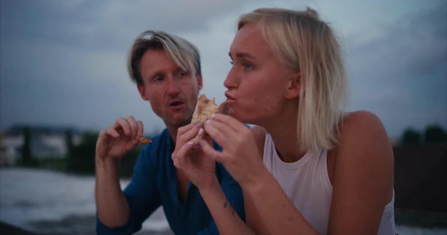 A happy young couple having a conversation while eating pizza outdoors