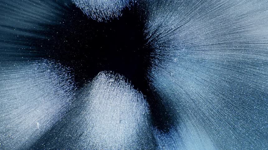 A white and blue liquid expands towards the camera against a dark background