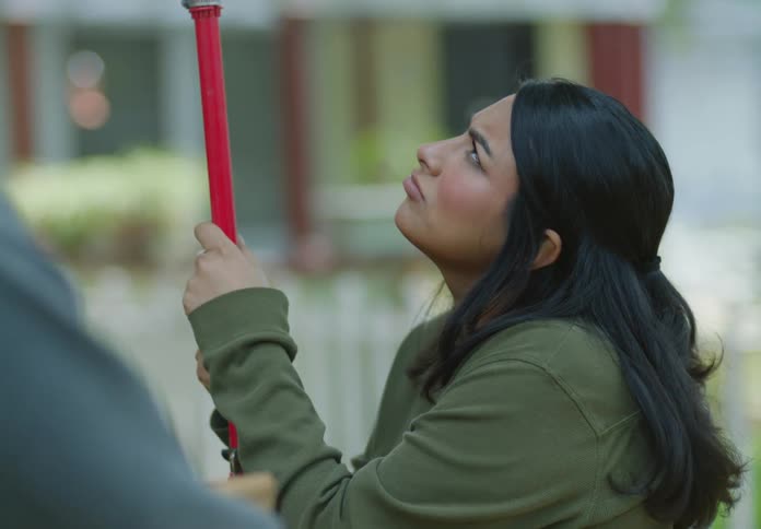A woman is holding something up in the air with a metal rod while talking and laughing to someone beside her holding a basket