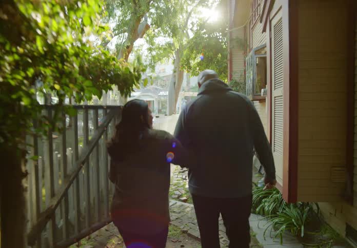 Couple walks through side yard of house arm in arm smiling and talking