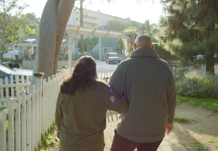A man and a woman back to back are walking together out of a house into the backyard and then hug each other