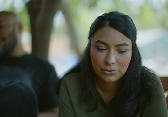 A middle eastern father and daughter talk while sitting outside under a tree