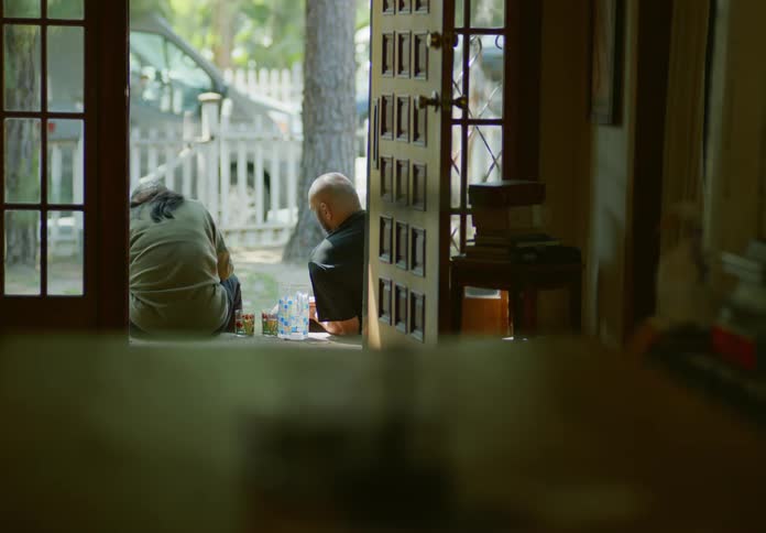 Two people are sitting on the floor near the front door of a house and one of the people is playing with a dog