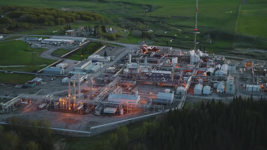 Oil and gas plant at dusk with orange work lights and green grass surrounding