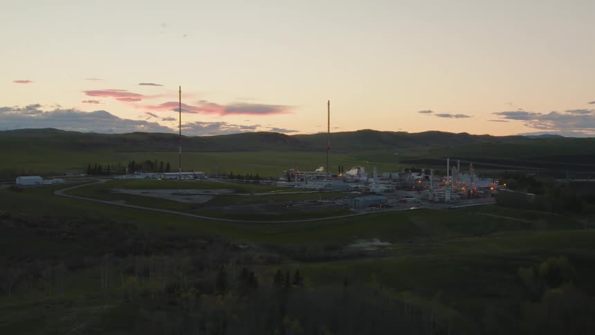 A refinery sits on a large grassy plain at dawn