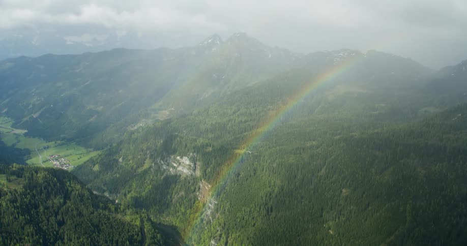 Aerial panorama of greenish mountain ranges and a long rainbow