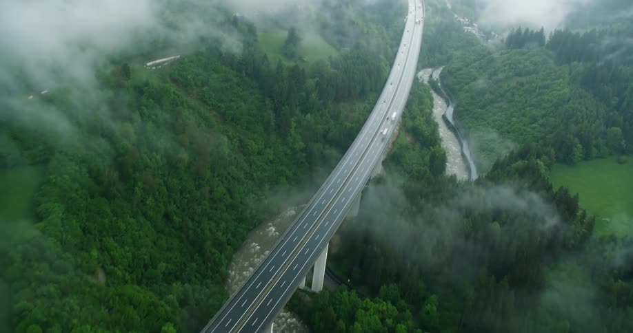 An aerial view of a highway with some cars passing by and on the sides there are many trees and green vegetation
