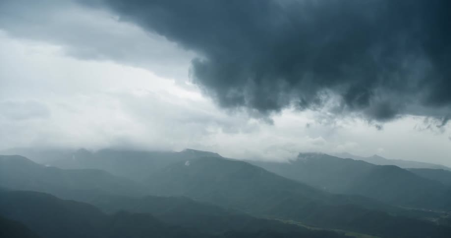 Dark clouds pass over foggy mountainous terrain