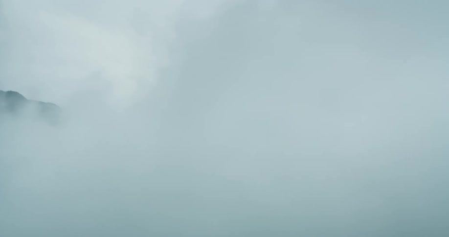 A dense white fog passing in front of a mountain peak
