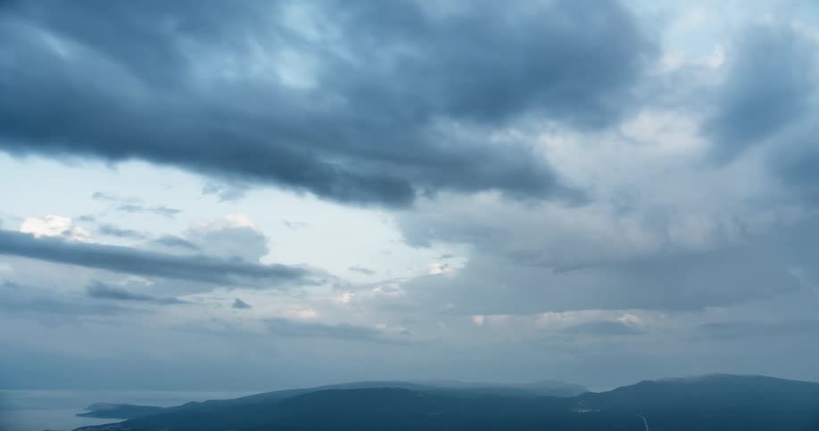 Dark clouds flow over misty mountainous terrain near the coast
