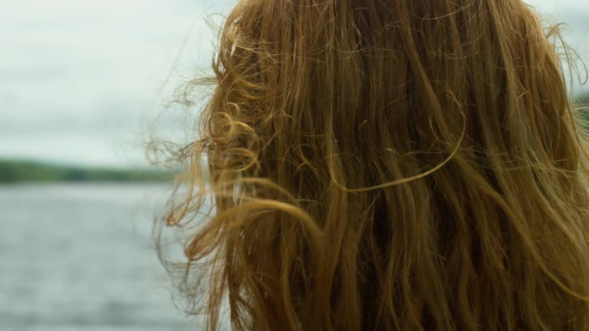 Red headed woman shakes her head while looking out over a lake