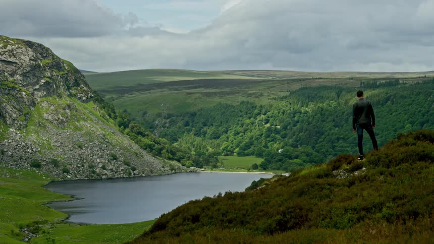 A man stands on a hill overlooking a lake