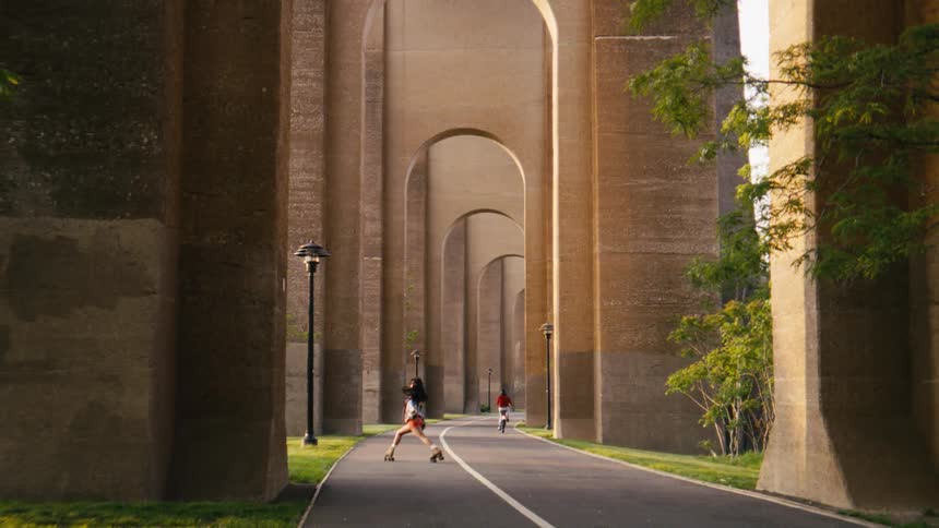 A woman roller skates on a path that runs underneath arched structures
