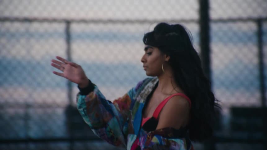 An indian girl dancing near a chain link fence