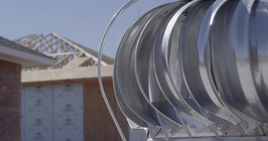 Silver metal vent spinning in front of a newly framed home