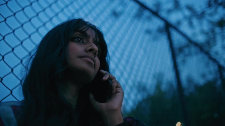 A woman talking on her smartphone stands in front of the fence at dusk