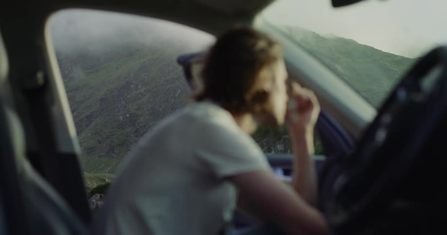 A man waiting in a car with an open door next to a mountain