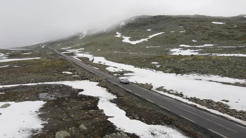 Aerial view of a car carefully driving on a snowy mountain road