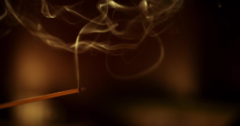 A hand holds a smoldering incense stick