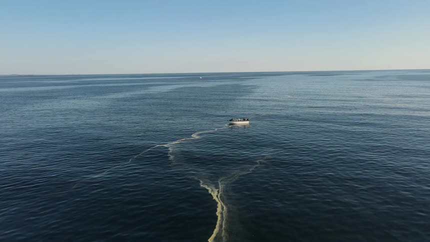 Boat with people in an extensive ocean against a cloudless blue sky