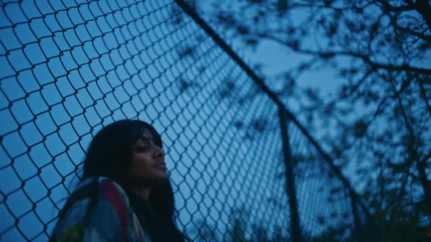 A woman leans on a fence by the tree