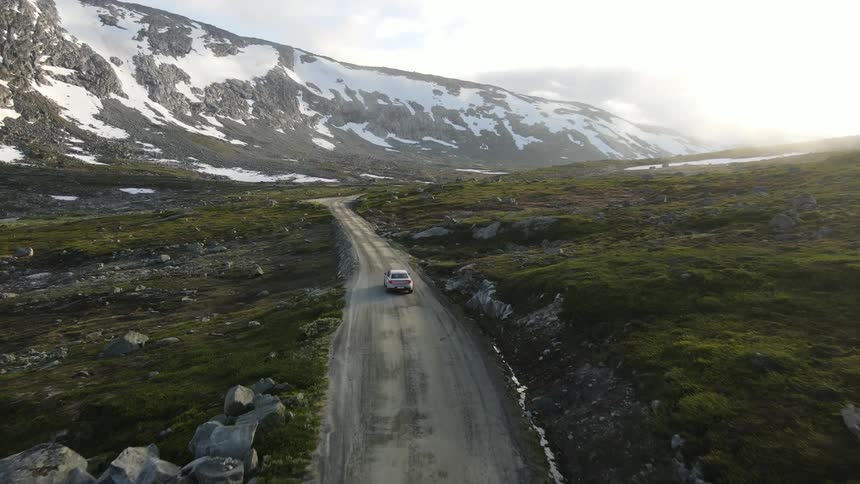 Aerial view of a car traveling along a road amid snowy hills and mountains