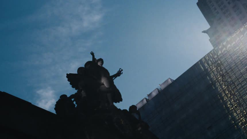 A large art deco statue with a woman holding a torch stands on top of a skyscraper