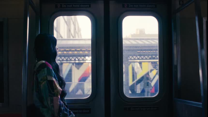 A woman standing inside a moving train looking out through the doors windows