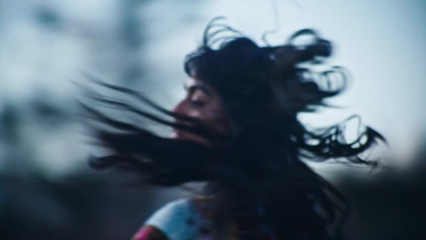 Portrait of a young woman with black hair walking and spinning in an outdoor setting with a blurred background